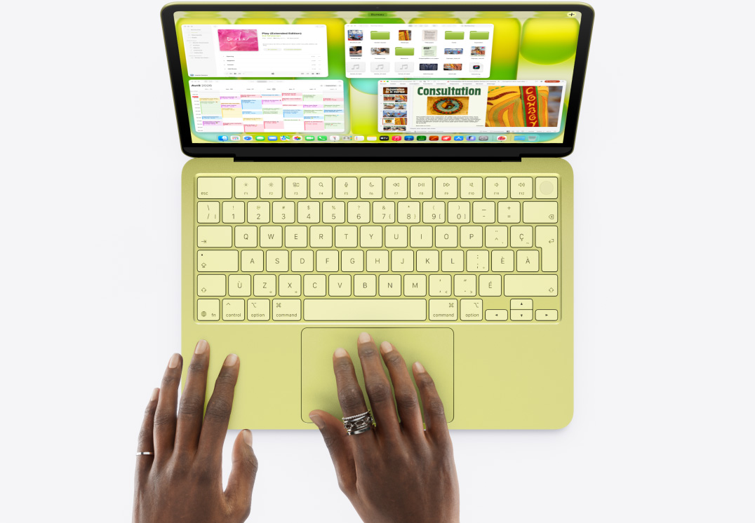 MacBook Neo, couleur agrume, des mains sur le pavé tactile, plusieurs fenêtres ouvertes, dont celles des apps Musique, Calendrier et Microsoft PowerPoint