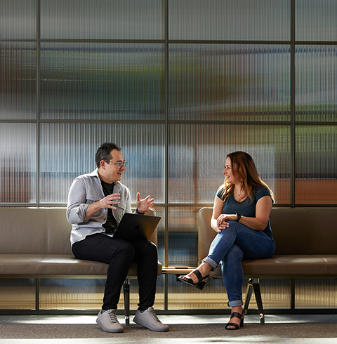 Two colleagues in conversation, sitting on benches in a common area.