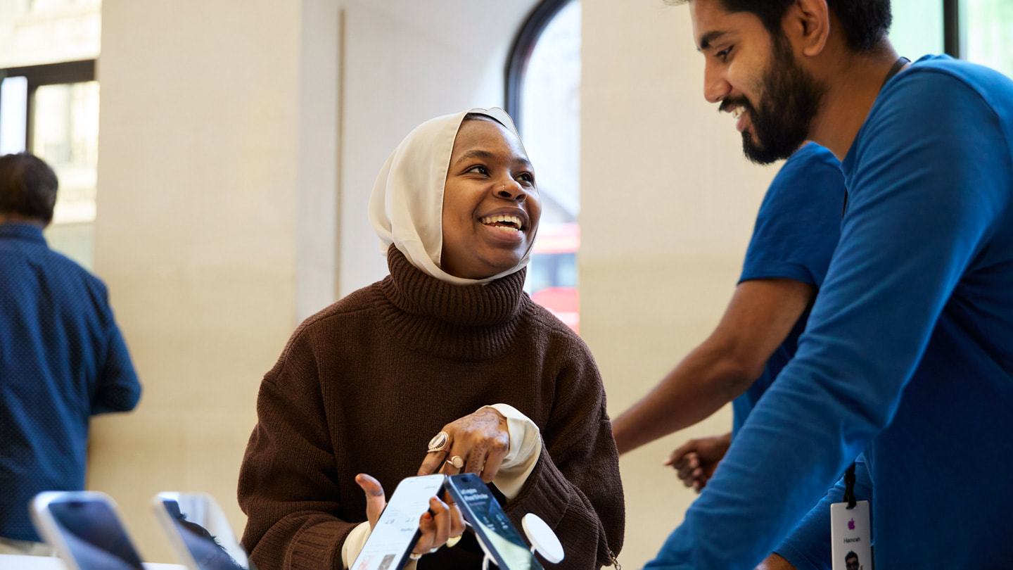 A customer holds iPhone 15 while talking to a team member at Apple Regent Street in London.