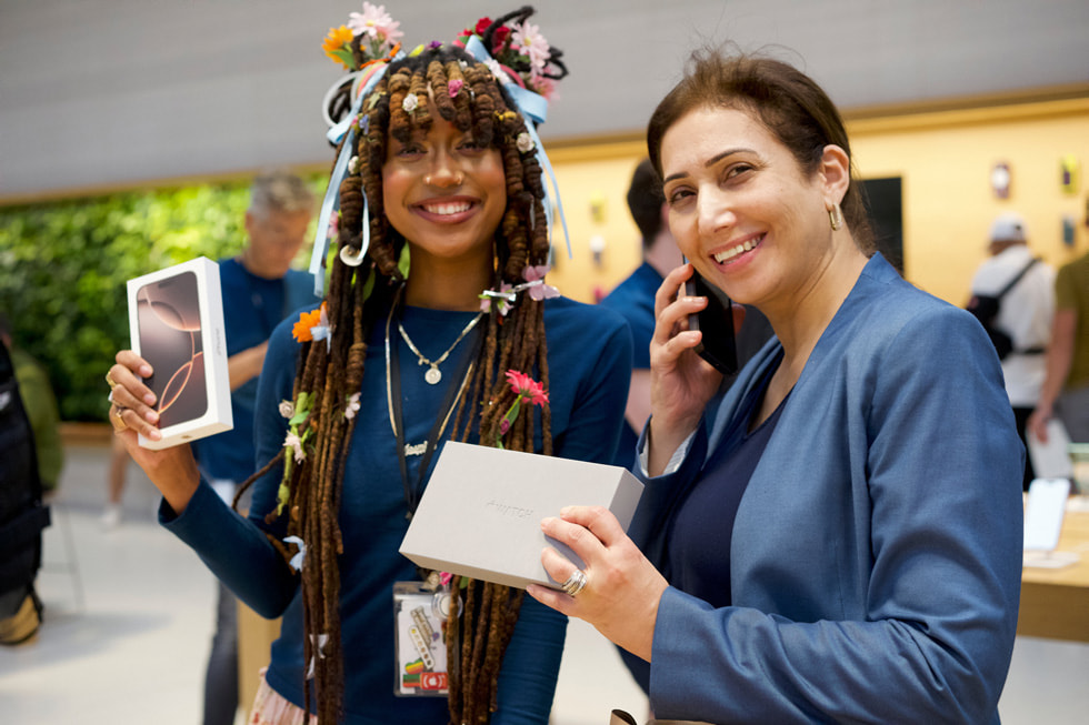 A smiling person holding an iPhone 16 Pro box stands next to a customer holding an Apple Watch box at Apple Fifth Avenue in New York City.