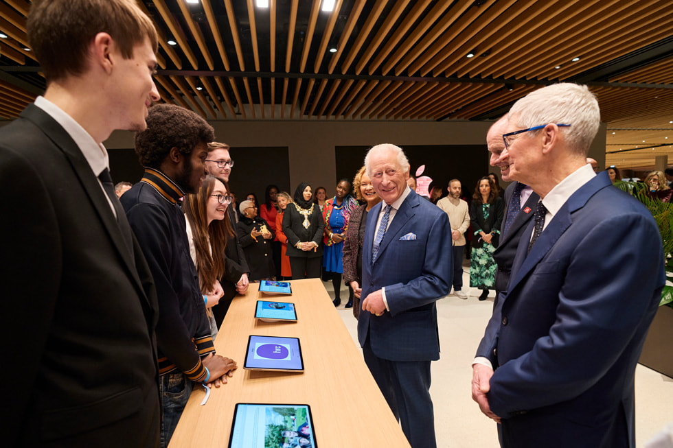 El rey Carlos y Tim Cook se encuentran con exalumnos de The King's Trust, que están de pie detrás de una mesa con dispositivos iPad.
