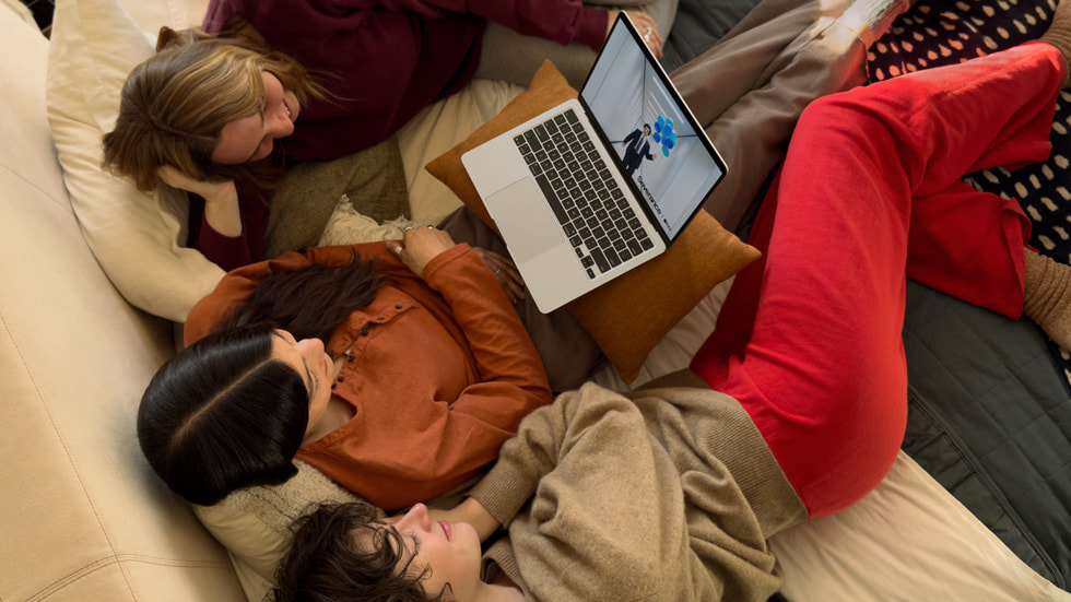 Three people watch “Severance” on MacBook Air while sitting on a couch.