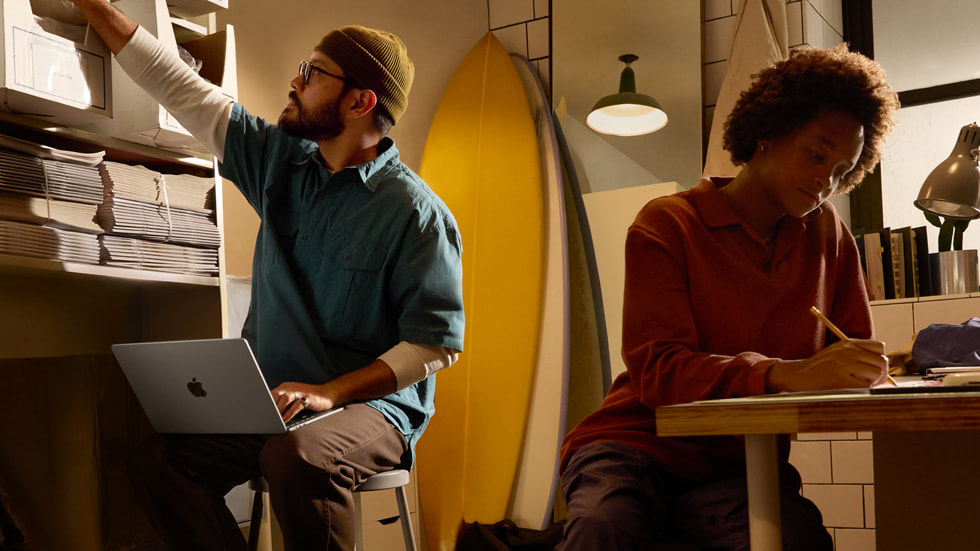 A Mac user holds MacBook Air while reaching for supplies on a shelf.
