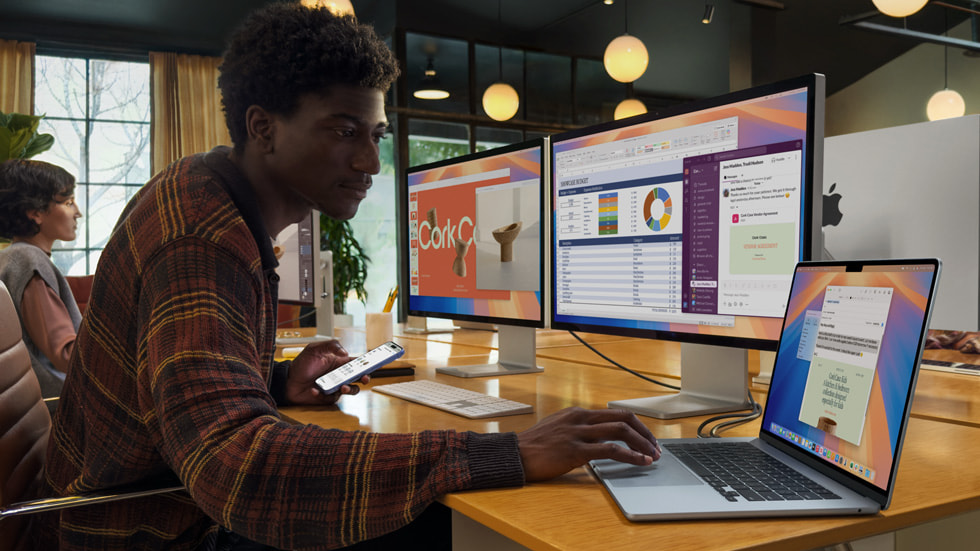 A person in an office setting is shown working with MacBook Air and two external displays.