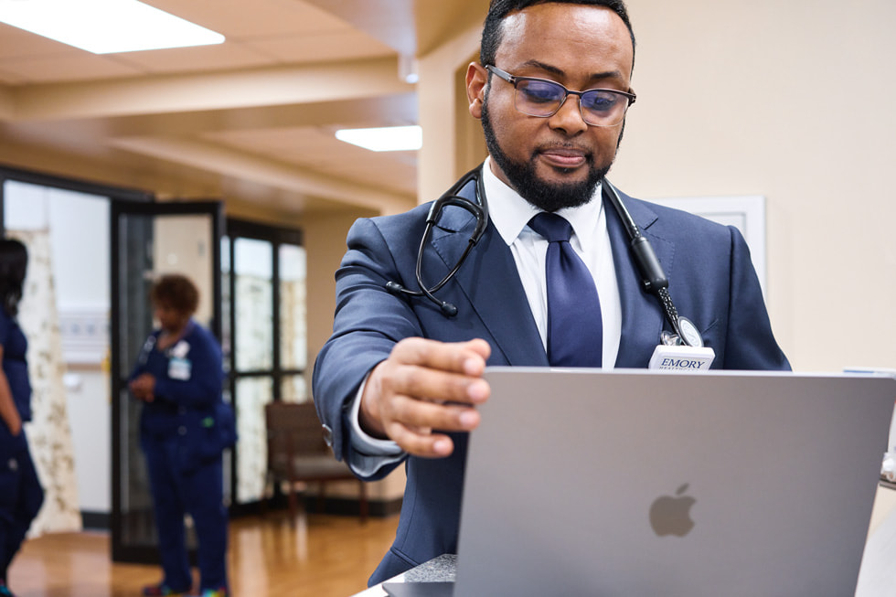 Dr. Yoseph Tekleyes holding a MacBook Air in the hallways of Emory Hillandale Hospital.