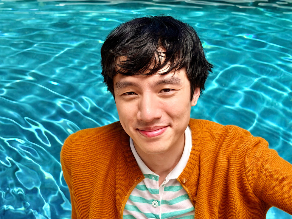 A portrait taken with iPhone 17 features a subject standing in front of colourful foliage.