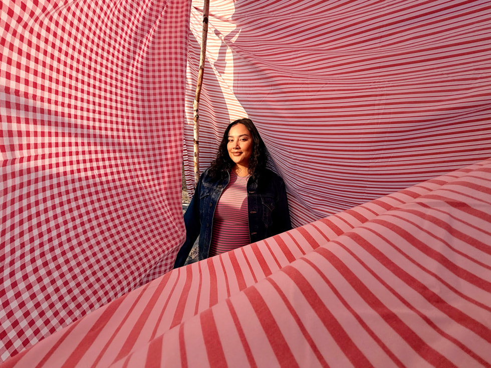 A photo taken with iPhone 17 shows a person standing in the middle of large pieces of fabric.