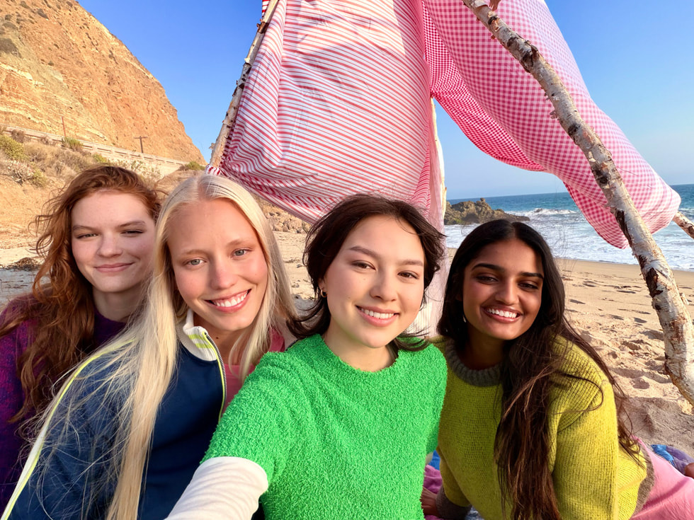 A group selfie taken with iPhone 17 shows four people at a beach.