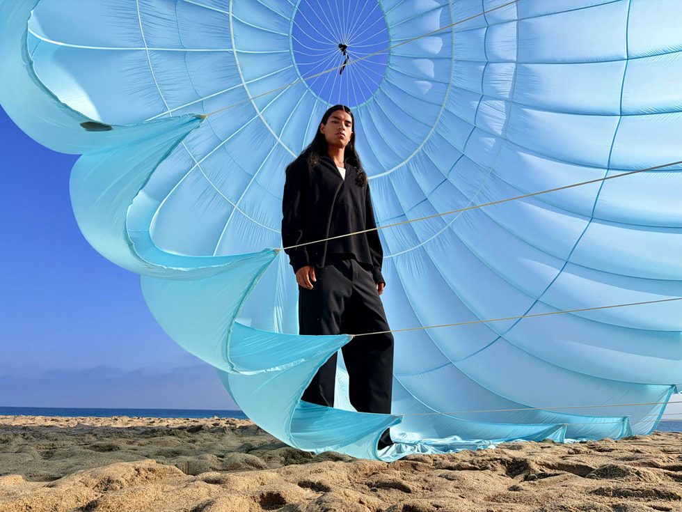 An outdoor photo of a person standing inside a hot air balloon billowing in the wind taken in 24MP on iPhone Air.