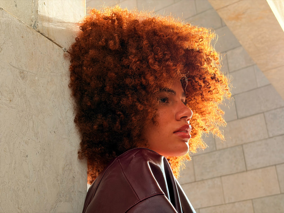 An outdoor portrait of a person with curly hair taken with 2x Telephoto on iPhone Air.