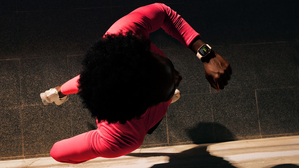 A person runs down a dark street, looking at their Apple Watch, where Workout Buddy is displayed.