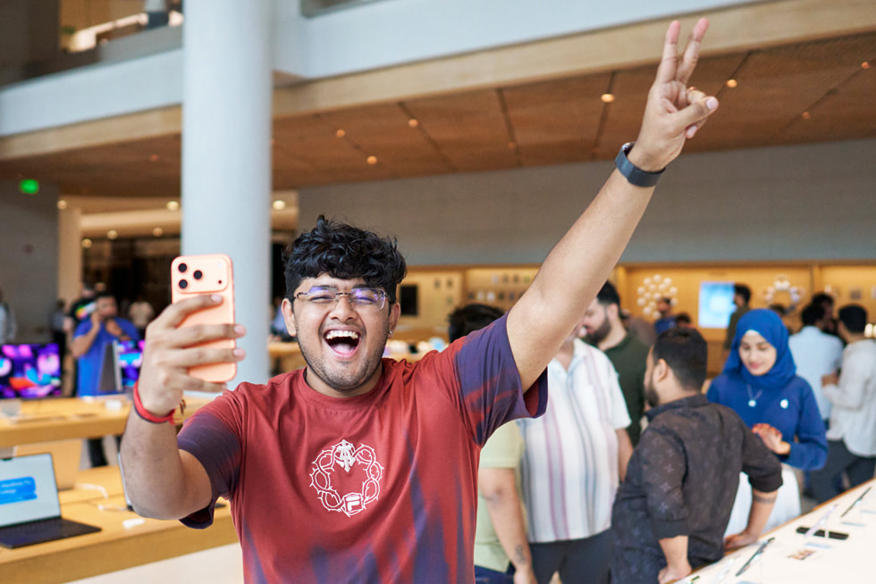 A smiling customer holds up their new iPhone 17 Pro purchase and makes a peace sign with their other hand at Apple BKC in Mumbai.