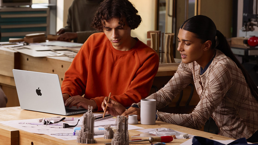 A lifestyle photo shows two people working with the new 14-inch MacBook Pro as well as various sketches and architectural models.