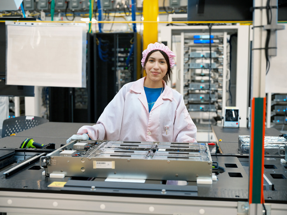 A worker in a lab coat stands behind an assembly line.
