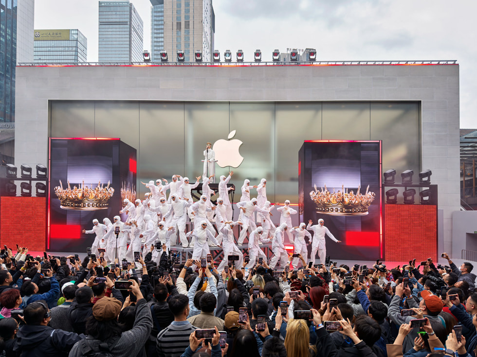 Tänzer:innen in weissen Overalls bilden eine Pyramidenformation, während Chris Lee an der Spitze in Apple Taikoo Li Chengdu in China singt.
