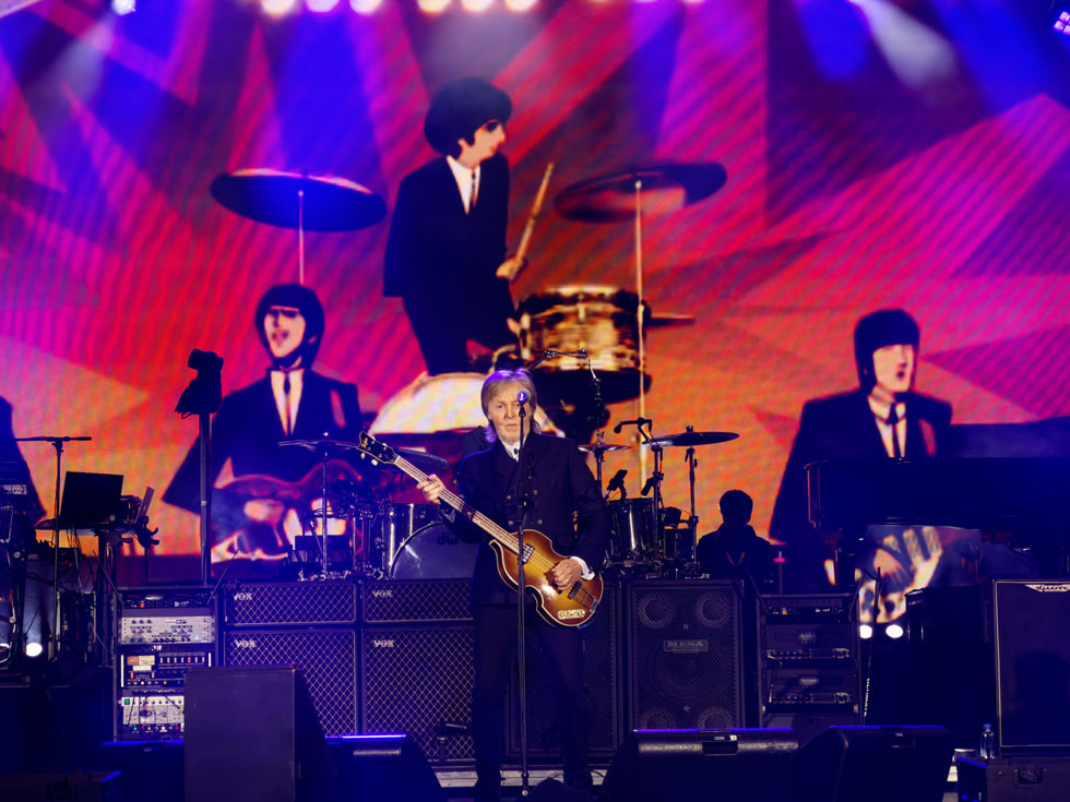 Paul McCartney is shown performing on stage at Apple Park in Cupertino with animated musicians representing members of the Beatles behind him.