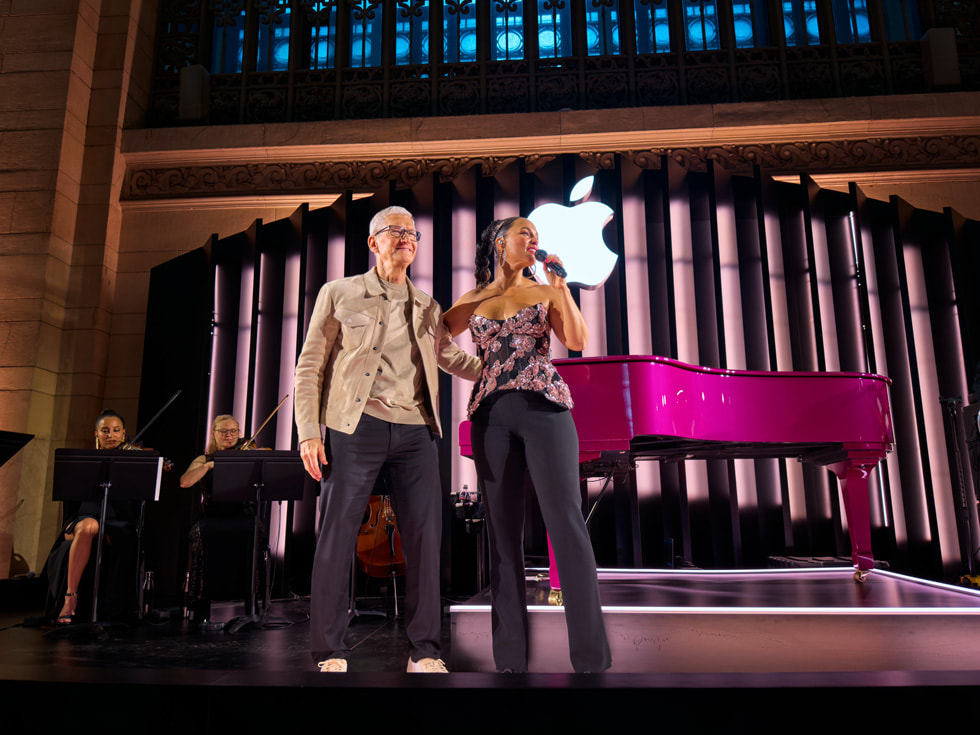 Tim Cook winkt, während er neben Alicia Keys auf der Bühne steht.
