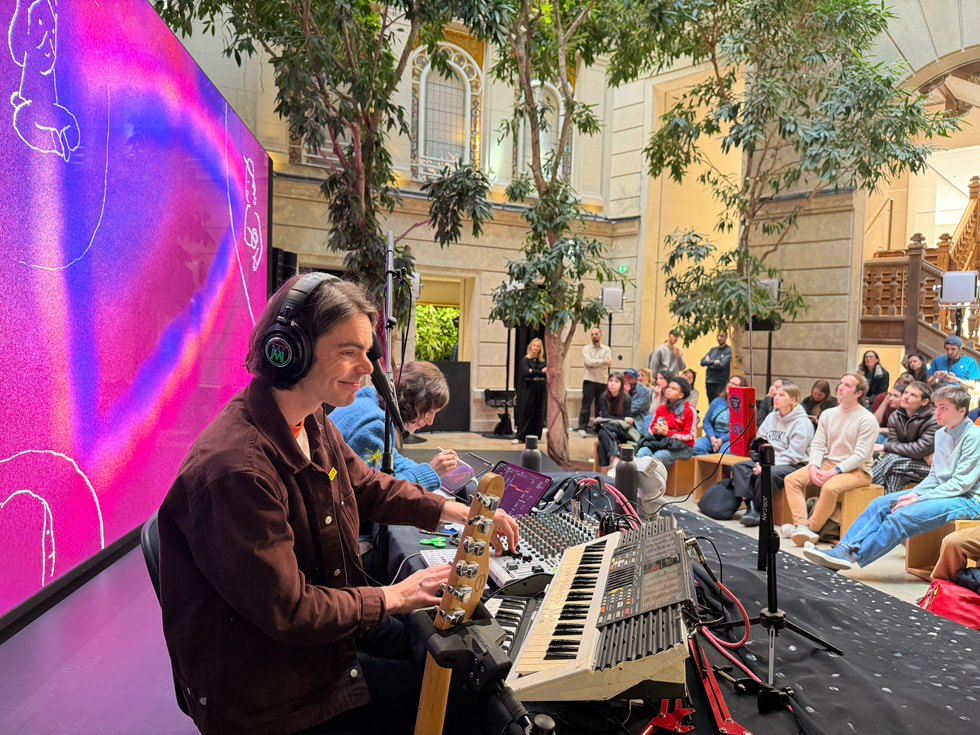 Pi Ja Ma draws on iPad while seated next to SOPORI FM in front of a large screen featuring an illustration at Apple Champs-Élysées in Paris.