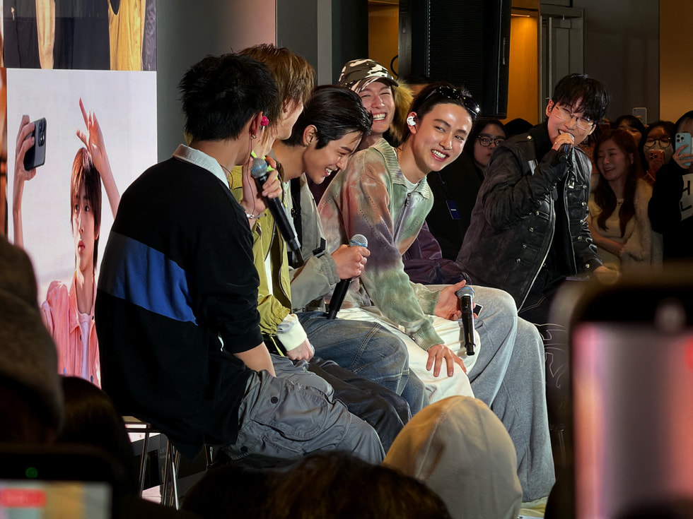 Die Mitglieder der Band CORTIS sind lächelnd und mit Mikrofonen in den Händen in Apple Myeongdong in Seoul abgebildet. 
