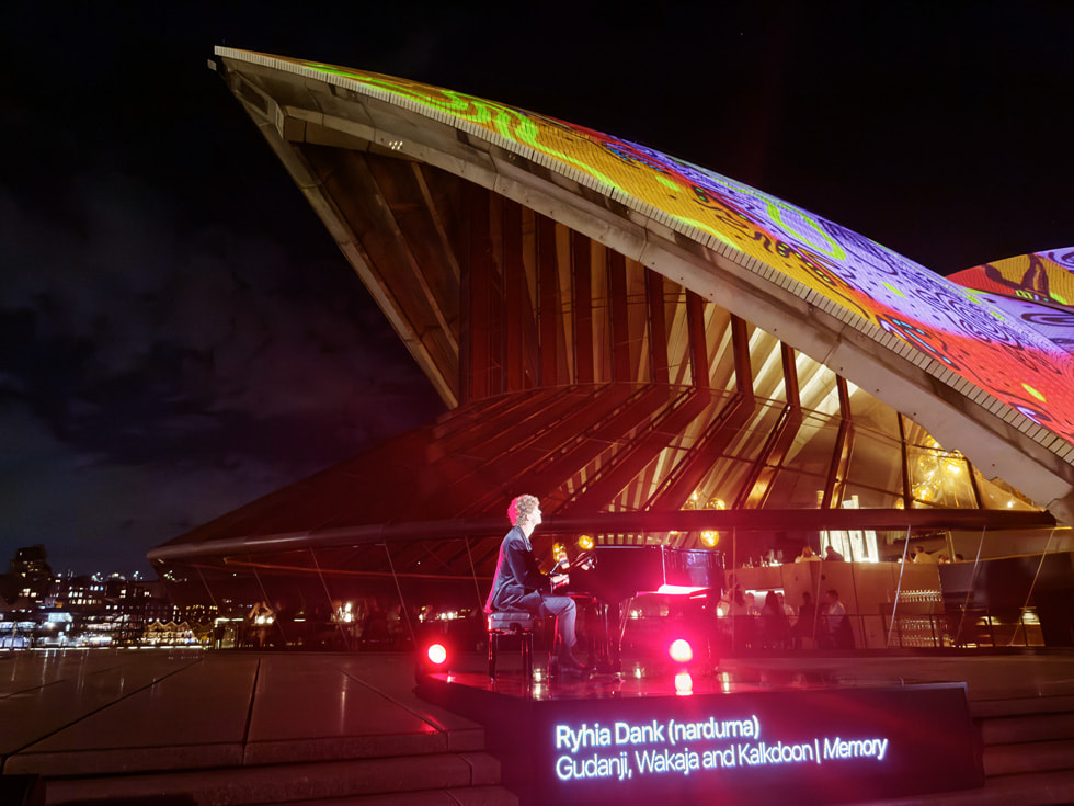 A performer plays piano in front of Apple’s Bennelong sails projection installation.