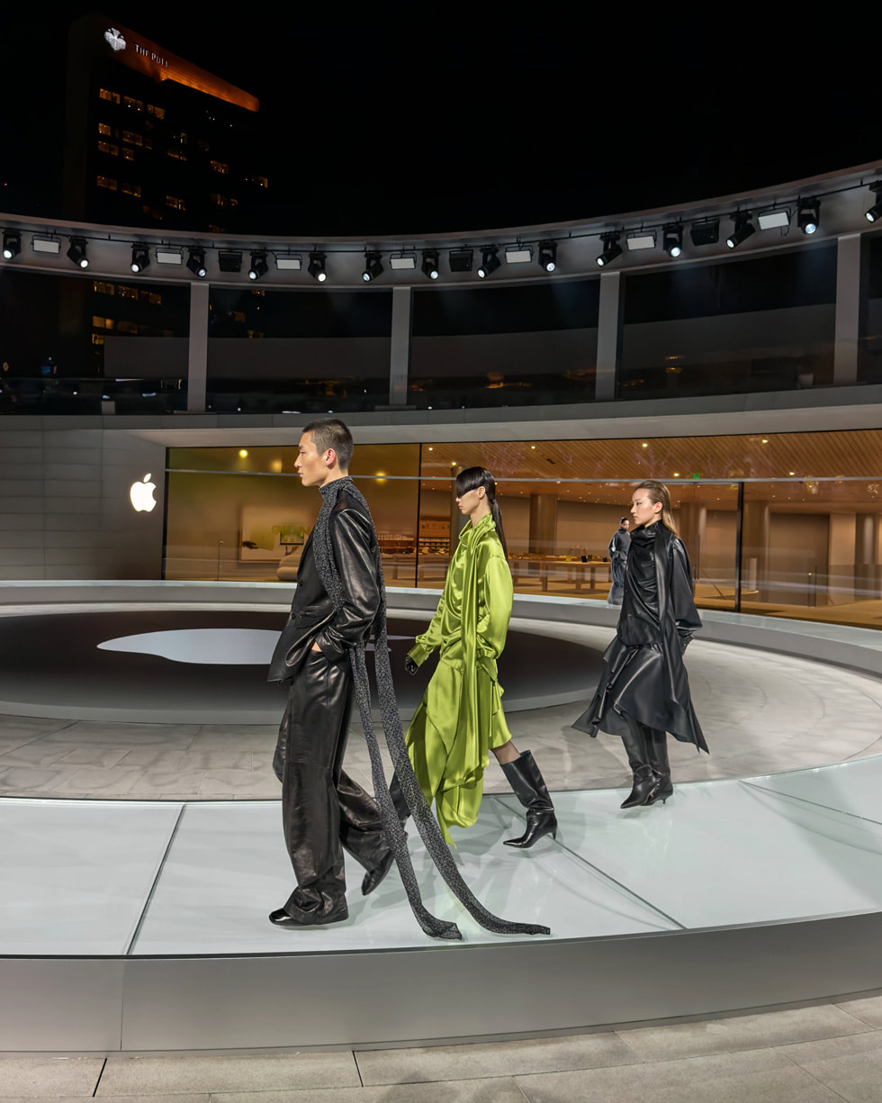 Two models dressed in black and one in green walk a circular runway at Apple Jing’an.