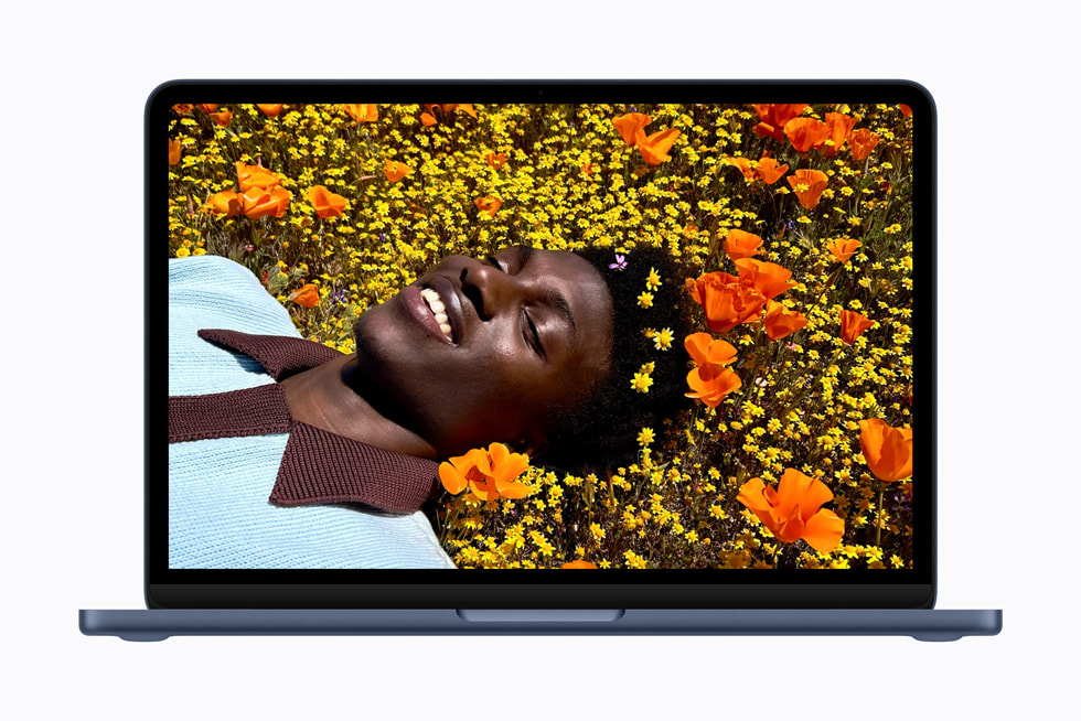 Una MacBook Neo índigo abierta muestra una foto colorida de una persona acostada en un campo de flores.