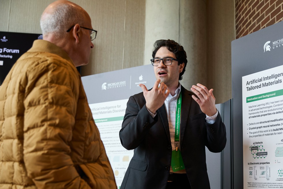 Dos participantes del Spring Forum conversan de pie frente a un póster titulado “Artificial Intelligence for Tailored Materials Discovery”.