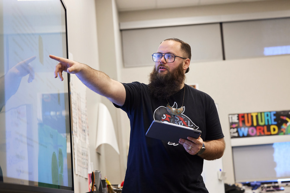 Tyler Teague is pictured holding iPad and pointing to a screen in a classroom.