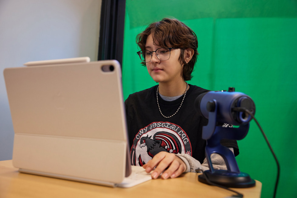 A student is pictured working on iPad with a microphone also on the desk.