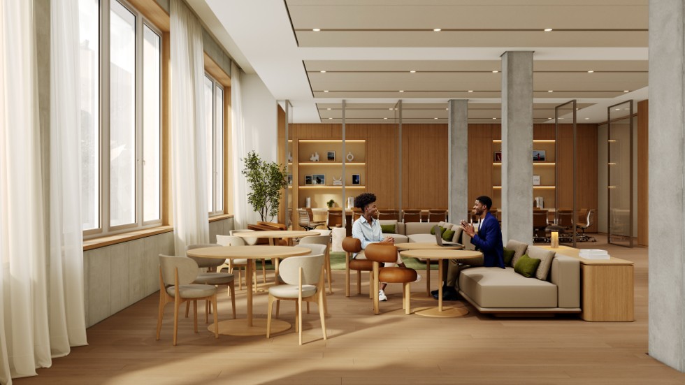 Několik lidí se sešlo v moderní, prosvětlené odpočinkové zóně s dřevěným nábytkem, stoly, židlemi a pohodlnou pohovkou