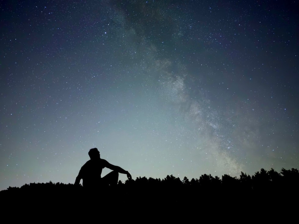 A photograph captured on iPhone 18 Pro using Night mode shows a person silhouetted against a starry sky.