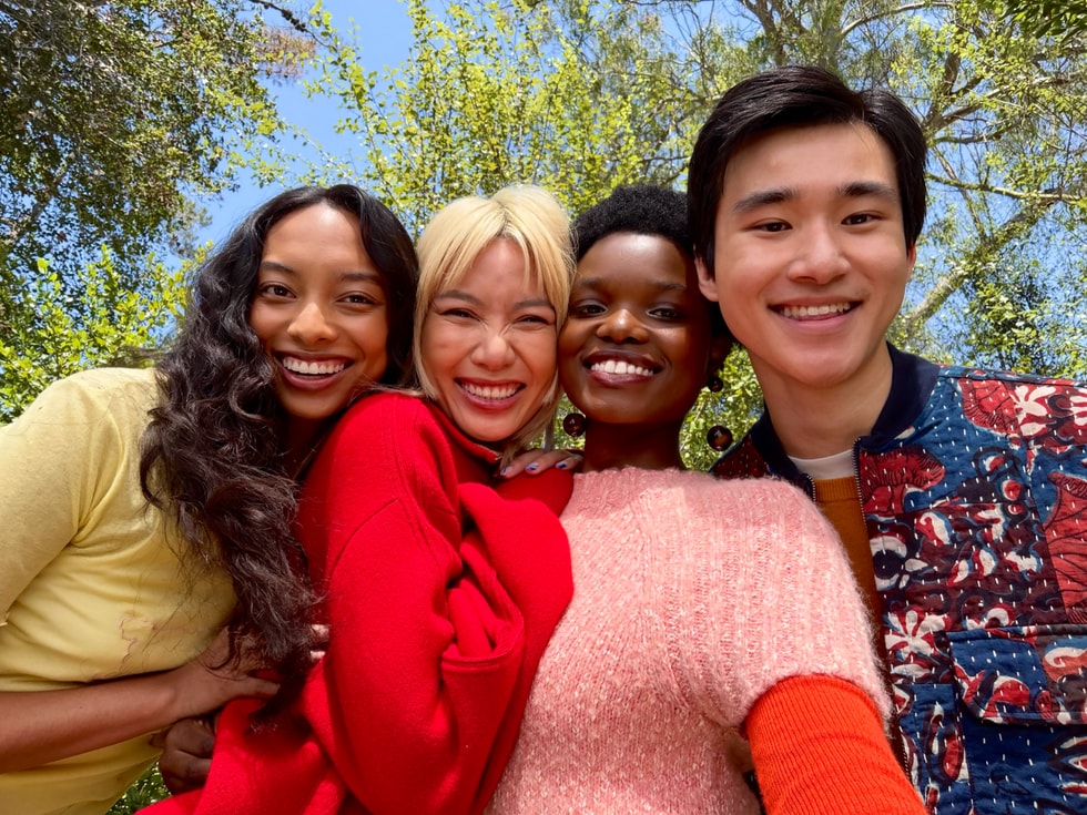 Four people smile and pose for a selfie outdoors.