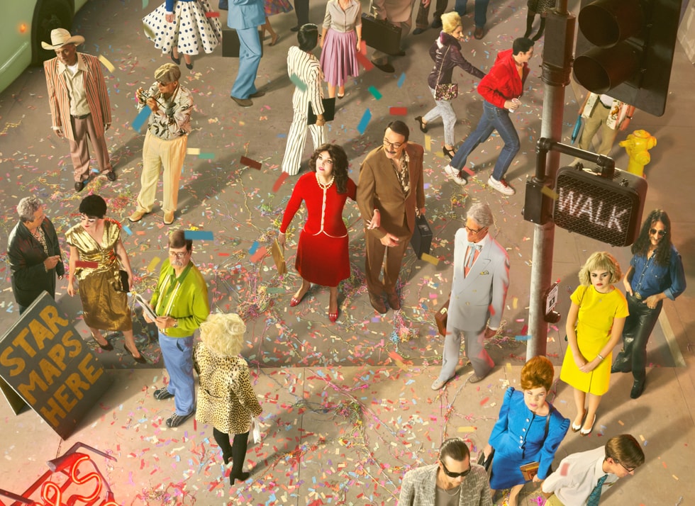 A photo shows people walking in a city scene with confetti on the ground and a “Star Maps Here” sign on the sidewalk as well as a walk sign. 
