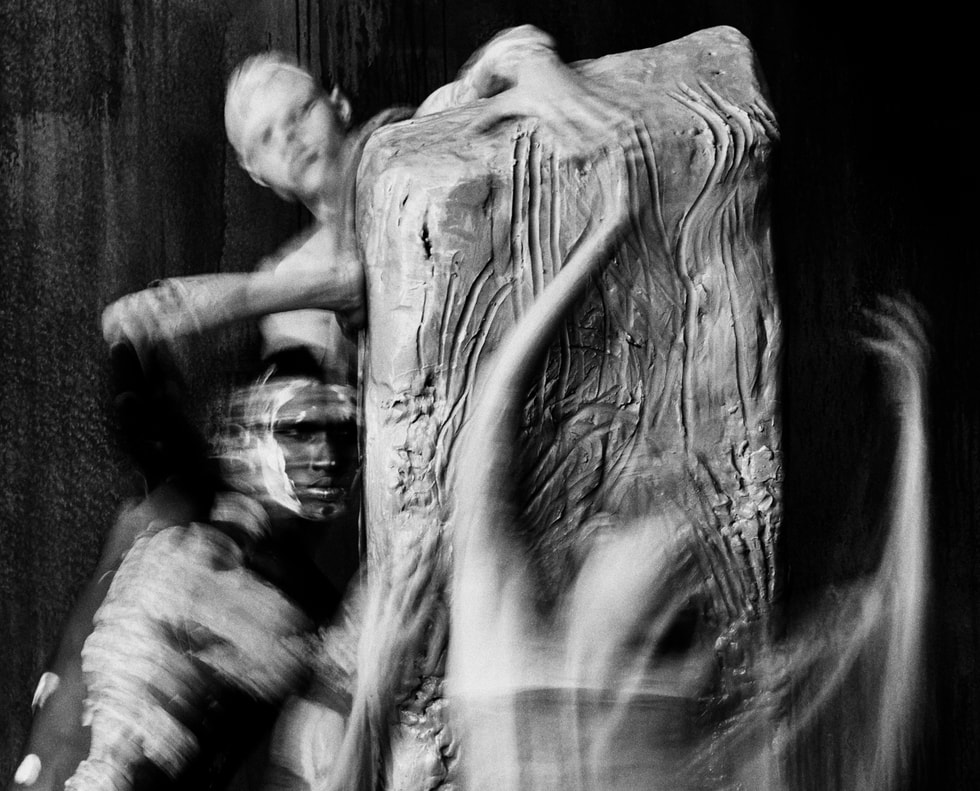 A photo shows multiple people touching clay.