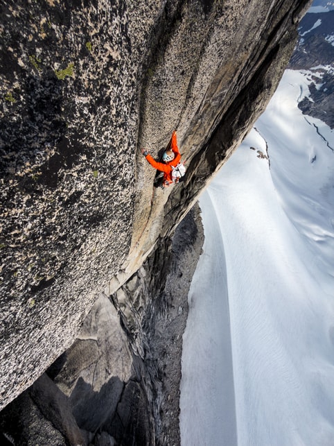 A climber is pictured clinging to the side of a steep mountain, with snow below them.