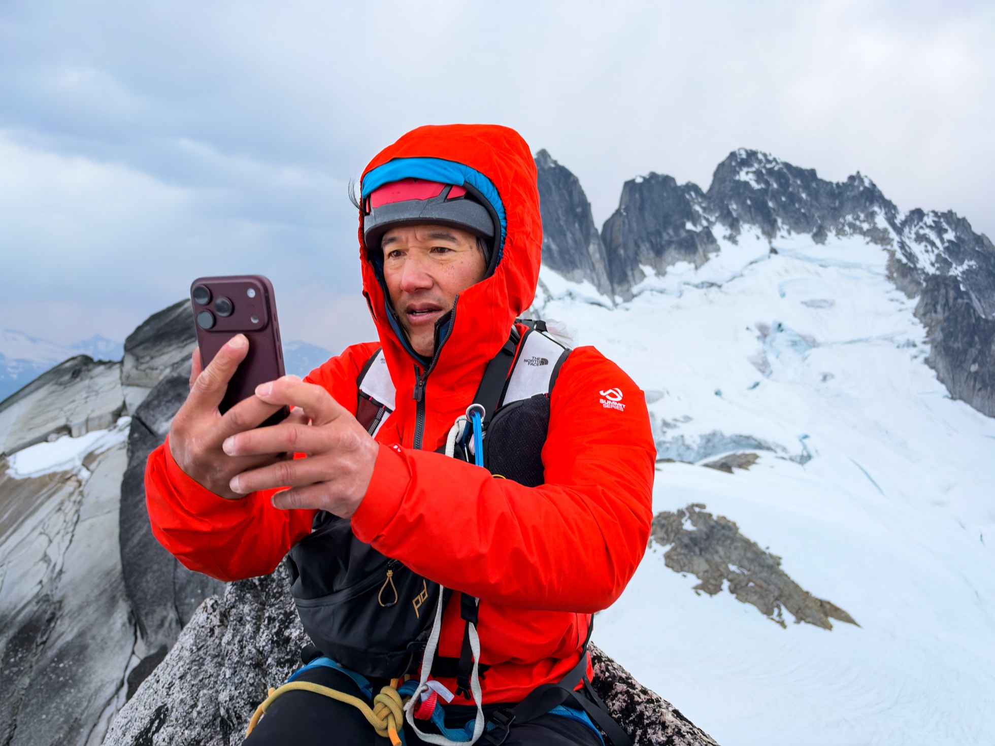Photographer Jimmy Chin is shown wearing climbing gear and holding iPhone 18 Pro on a mountaintop.
