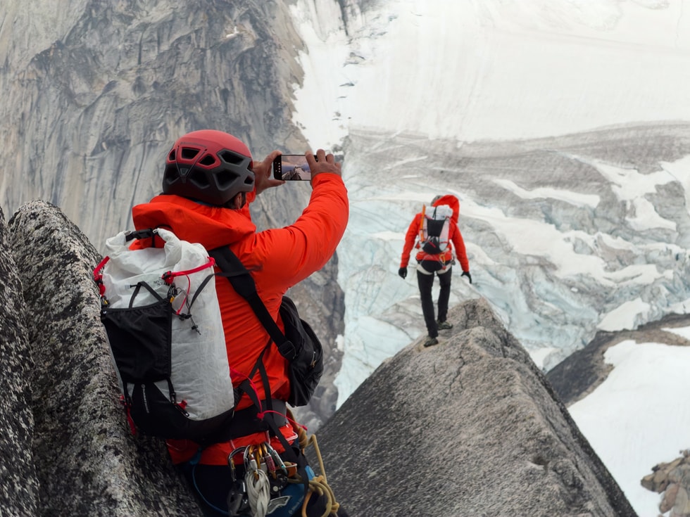 Photographer Jimmy Chin is shown wearing climbing gear and holding iPhone 18 Pro while taking photos of a climber.