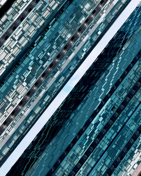 An angular close-up on the intricate windows of twin skyscrapers in Kuala Lumpur, with a sliver of cloudy sky in between.