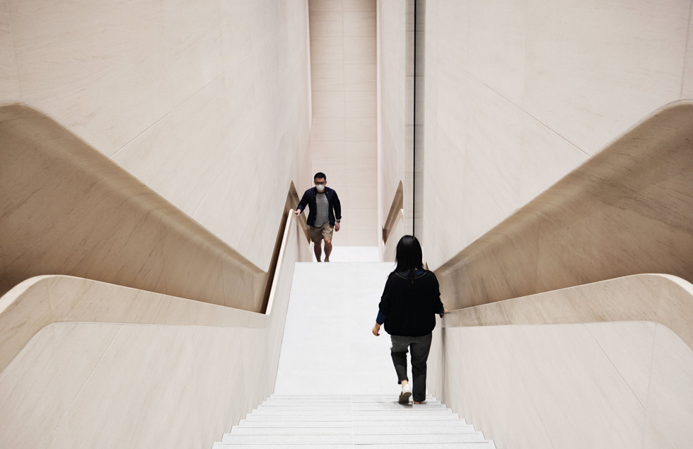 Two visitors, one wearing a face mask climbing up while another descends, on one of the store’s staircases.