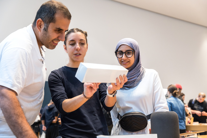 An Apple team member shows two customers details on an Apple Watch Series 4 box.