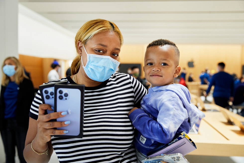Customer showing off her two iPhone 13 Pro purchases with her baby inside Apple Bay Plaza.