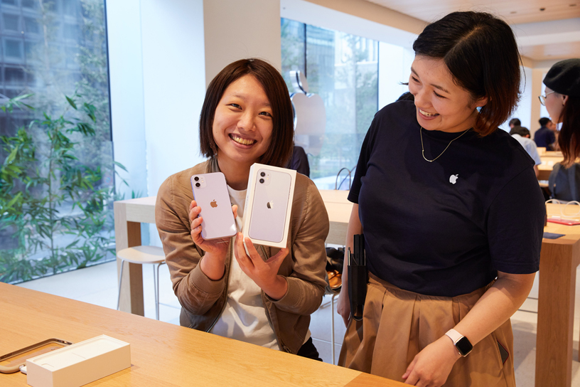 Customer holding up iPhone 11 and box next to an Apple team member at Apple Marunouchi.