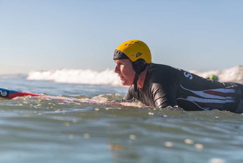 Leason sitting on surfboard in the water.