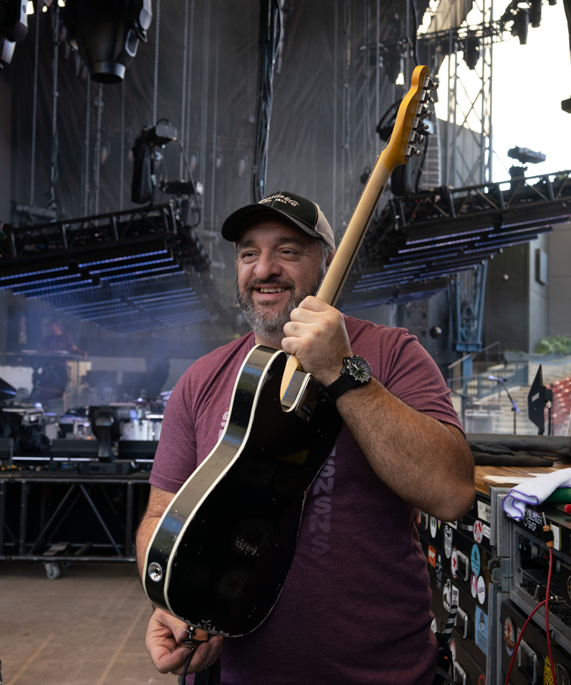 Guitar tech Carlos Gutierrez holding a guitar back stage.