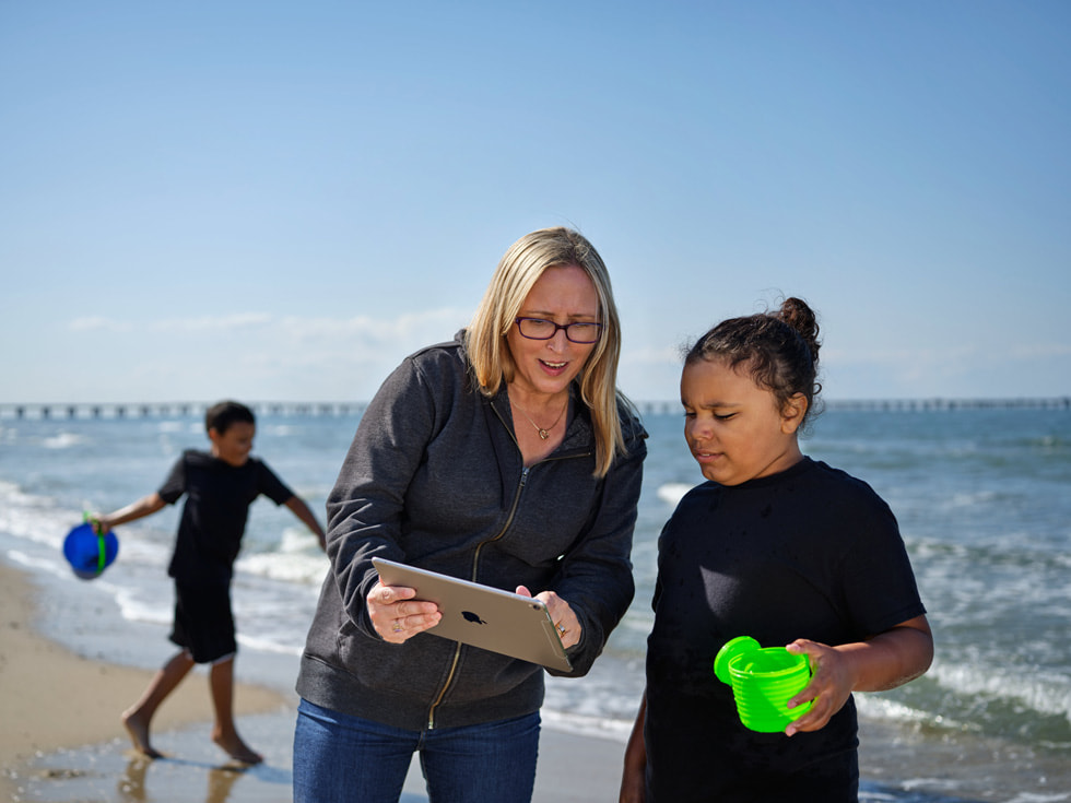 Jay’s mother Meghan and Jay using iPad, with Nick playing in the water behind them.