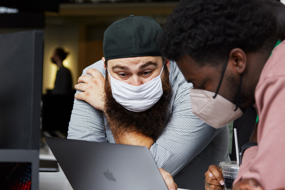 Two mentors using a MacBook to teach inside the Detroit Apple Developer Academy.