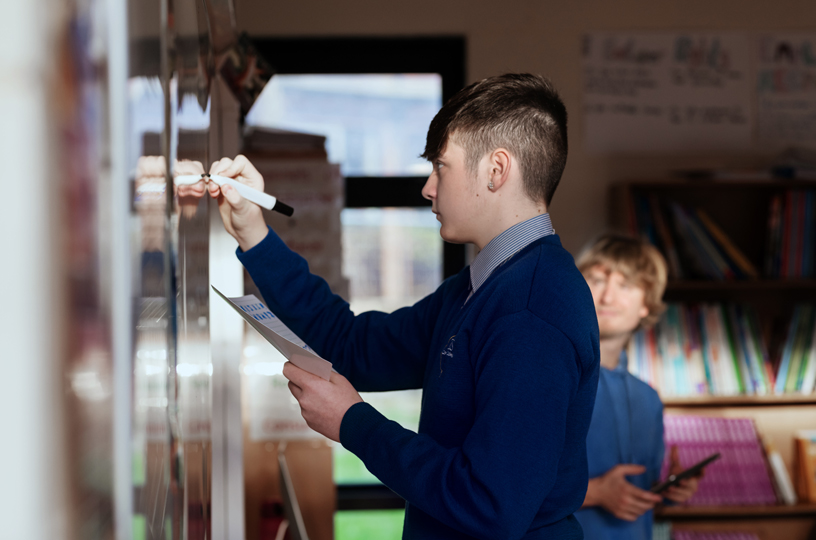 A student writing on a whiteboard at Terence MacSwiney School.