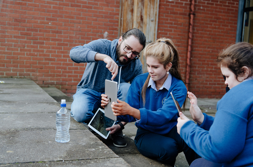 A young woman uses iPad to shoot a photo, with help from an Apple volunteer.