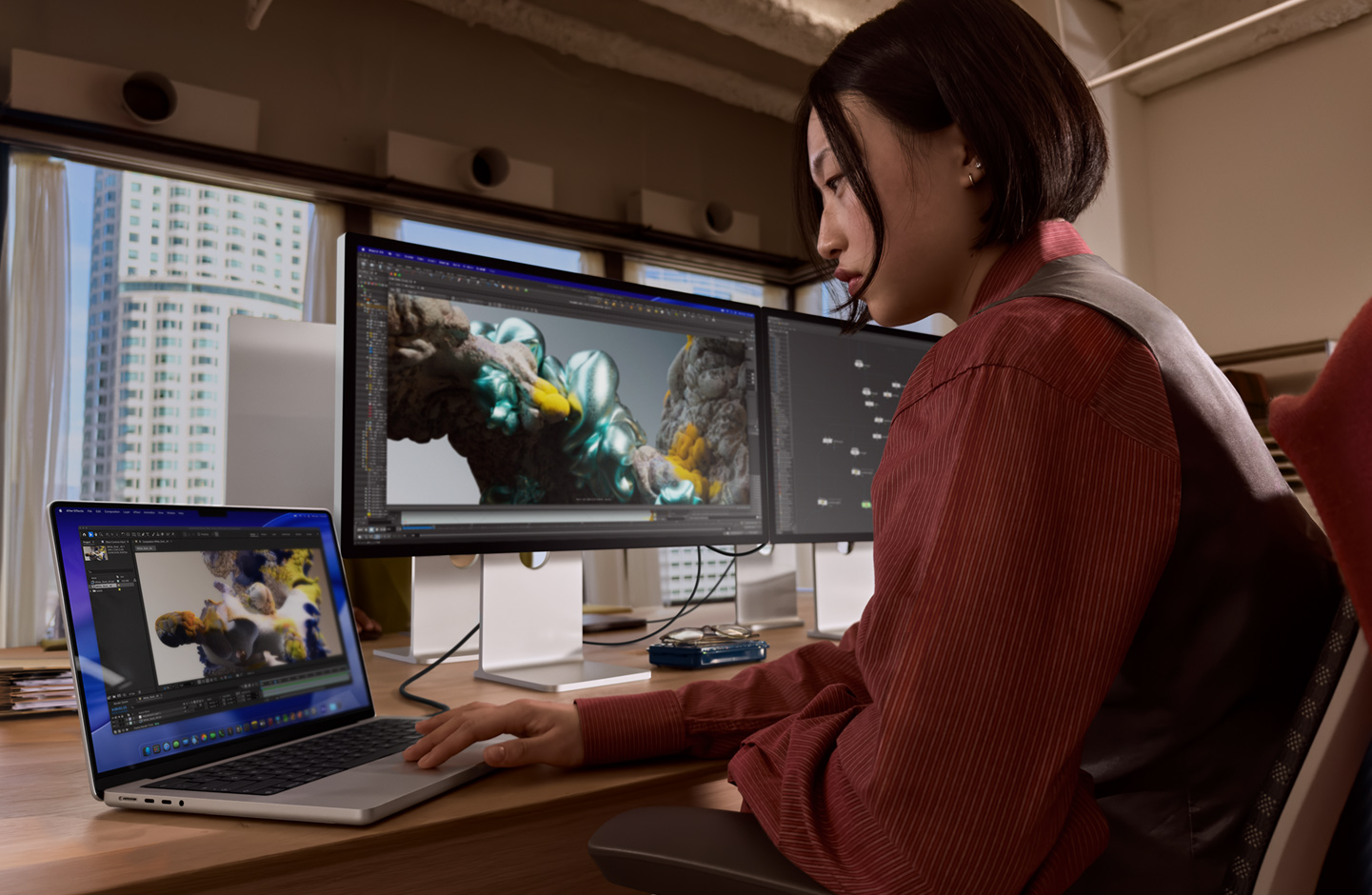 A person in an office setting works on a MacBook laptop that is connected to Studio Display XDR by a Thunderbolt 5 port