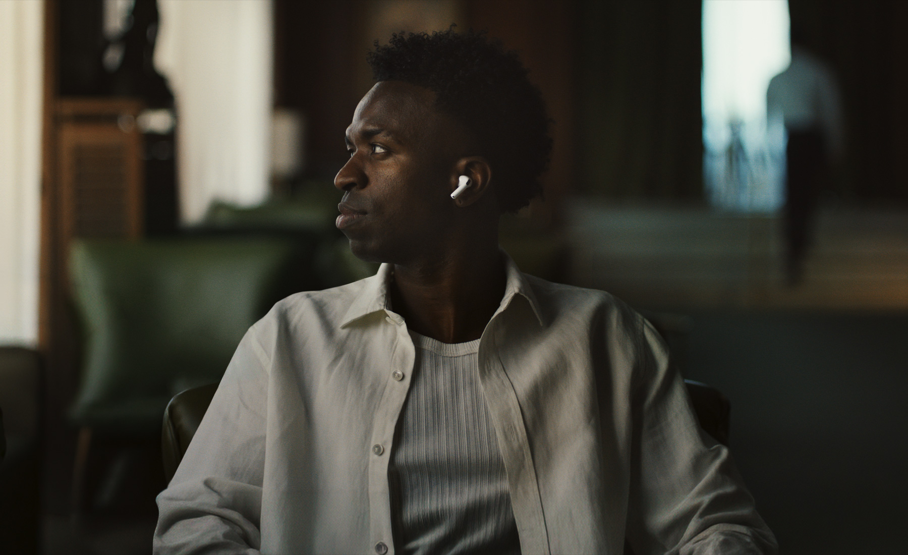 Una persona con una camisa blanca, cabeza girada hacia un lado, se ve el auricular izquierdo de unos AirPods Pro 3